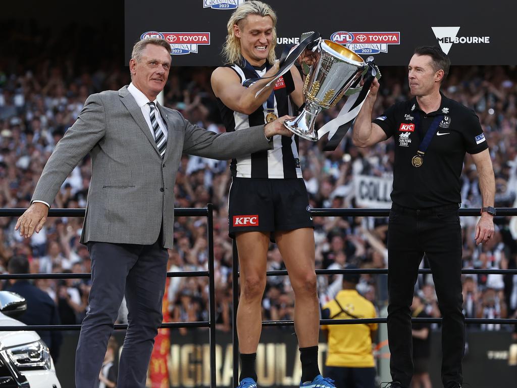 Collingwood captain [PLAYERCARD]Darcy Moore[/PLAYERCARD], centre, and coach [PLAYERCARD]Craig McRae[/PLAYERCARD] receive the premiership cup from Darcy’s father Peter Moore (far left). Picture: Michael Klein