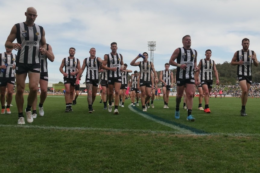 men in black and white footy jumpers walking off football field