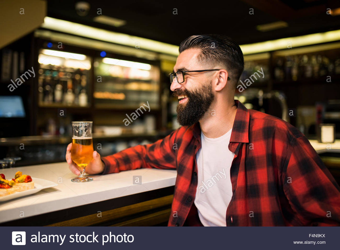 hipster-with-glass-of-beer-and-tapas-sitting-at-counter-in-a-pub-F4N9KX.jpg
