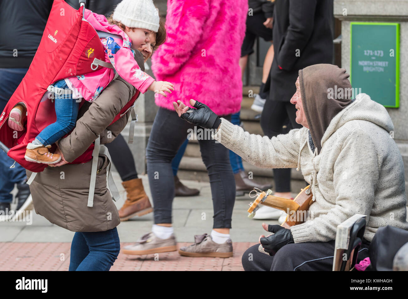 young-child-on-womans-shoulders-giving-money-to-a-street-busker-in-KWHAGH.jpg