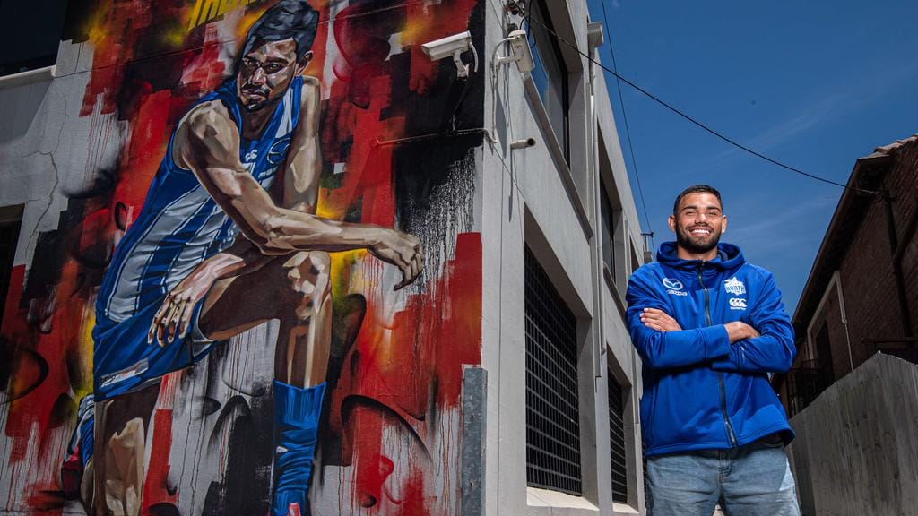 North Melbourne star [PLAYERCARD]Tarryn Thomas[/PLAYERCARD] in front of the Black Lives Matter Mural of him at the corner of Curzon St and Victoria St North Melbourne. Picture: Jason Edwards