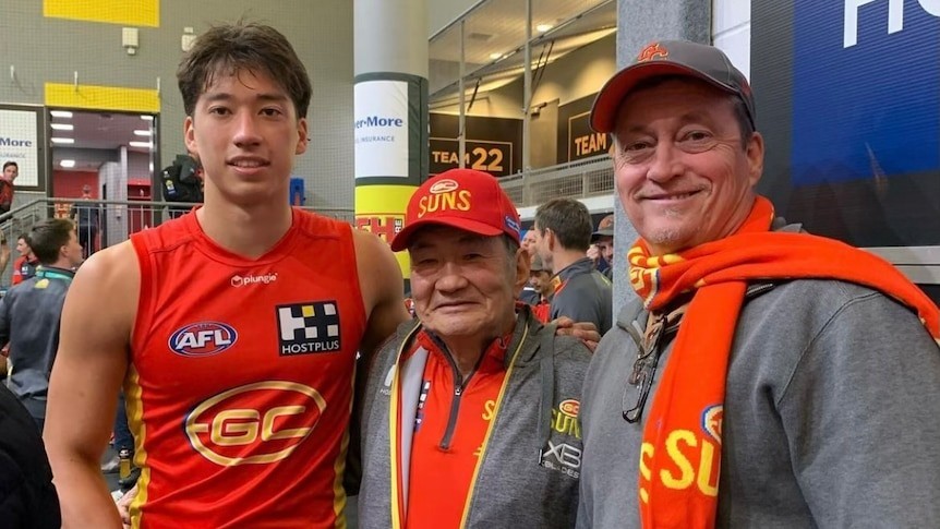 Two men pose with a player following an AFL debut
