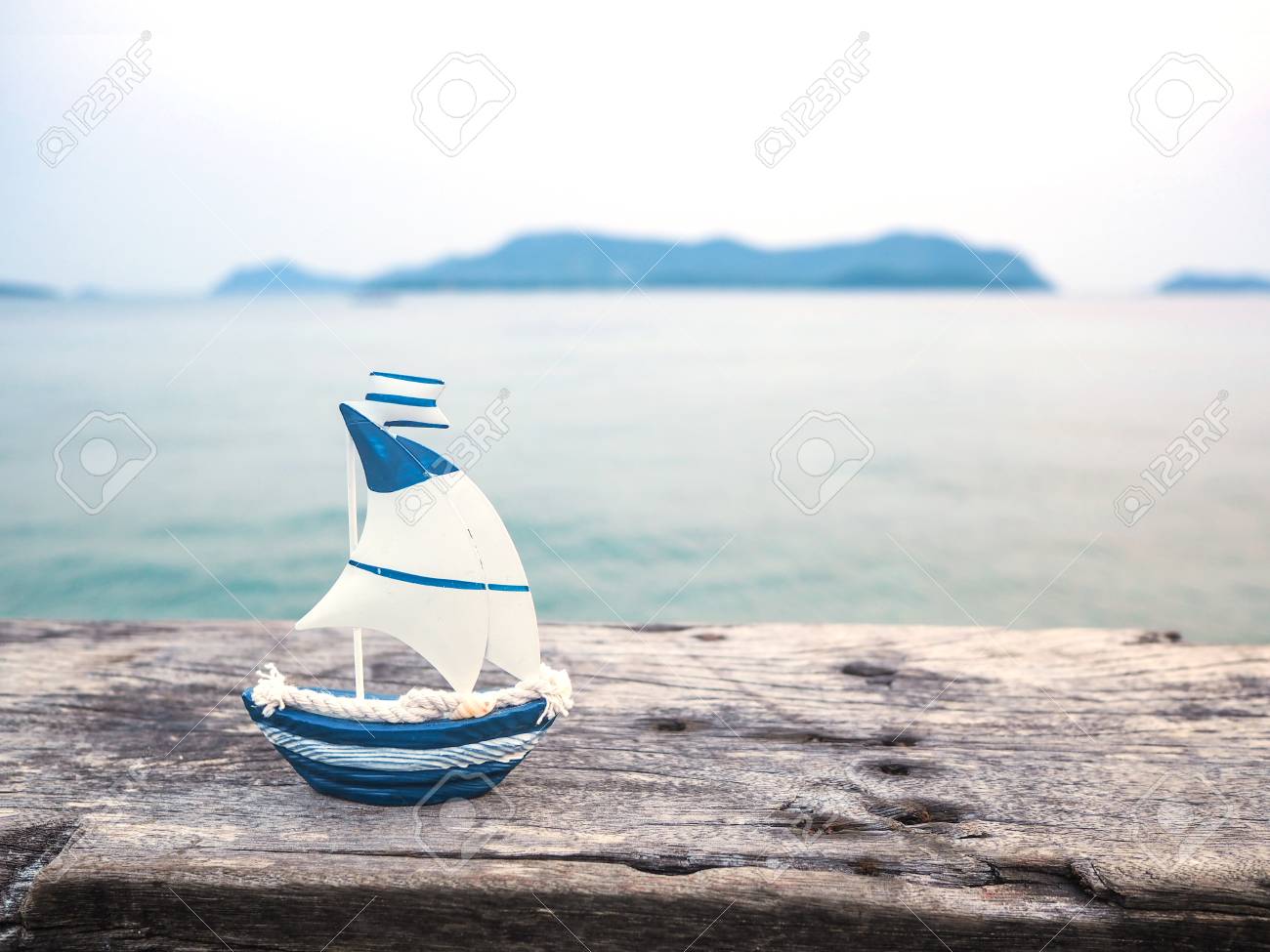 100897837-close-up-small-white-and-blue-boat-toy-on-wood-plank-over-sea-background-with-copy-space-vacation-on.jpg